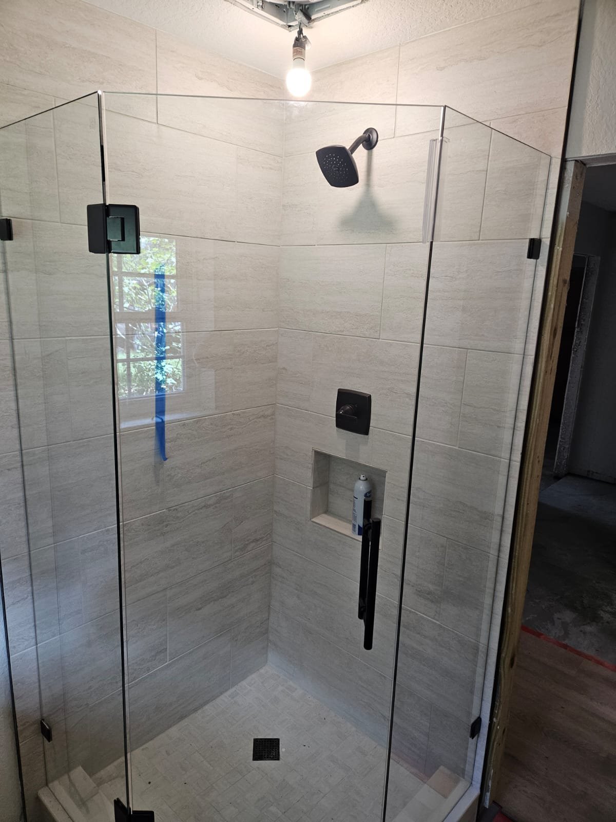 Ejemplo de baño en ángulo 135° SIN transom: la puerta de vidrio llega hasta arriba, sin panel fijo sobre ella, con herraje negro