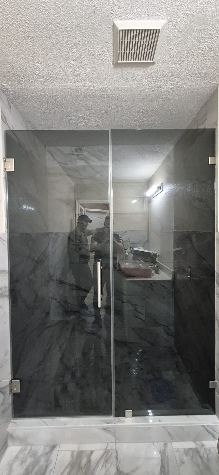Puerta de bisagras con vidrio Grey (gris ahumado), panel fijo y herraje brush nickel en shower de mármol oscuro
