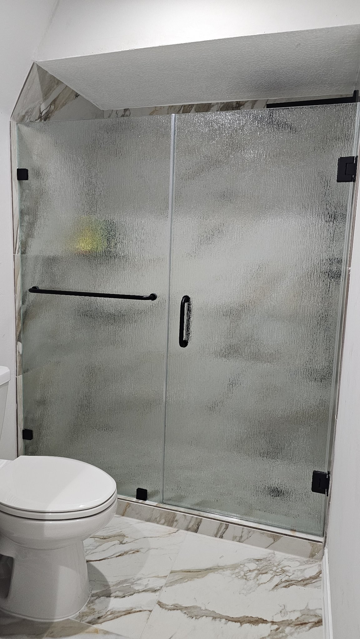 Puerta de bisagras a la pared con vidrio Rain (textura de lluvia), panel fijo con toallero y herraje negro en shower de mármol