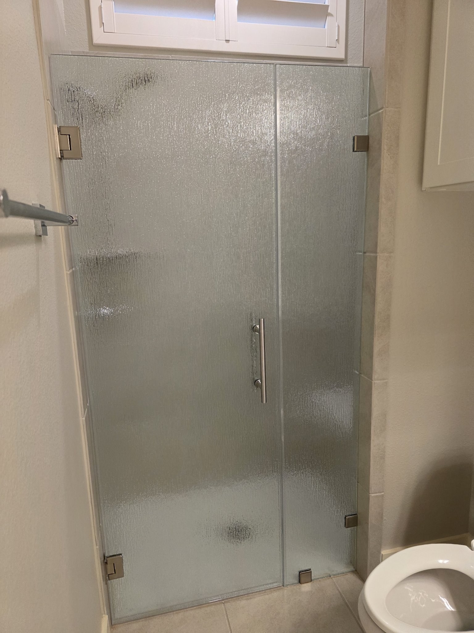Puerta de bisagras a la pared con vidrio Rain (textura de lluvia) y panel fijo, con herraje de níquel