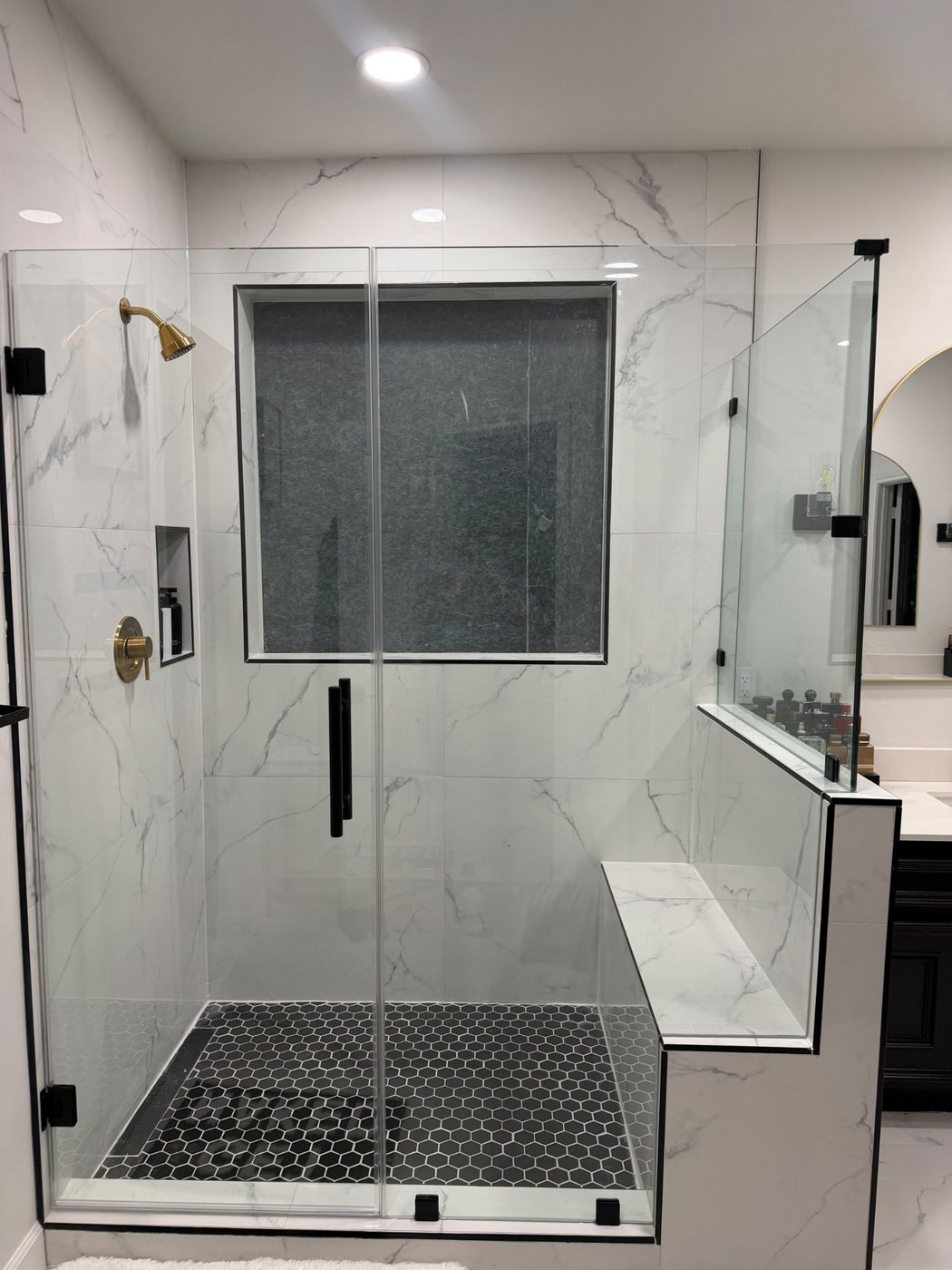 Trabajo de Glas Plus: ángulo 90° con herraje negro y el retorno de vidrio sobre un murete con banca, en un shower de mármol