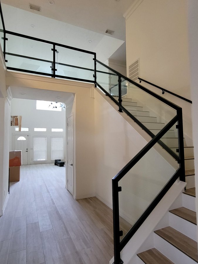 Ejemplo de escaleras de Glas Plus: barandal de vidrio con marco negro en escalera y balcón superior