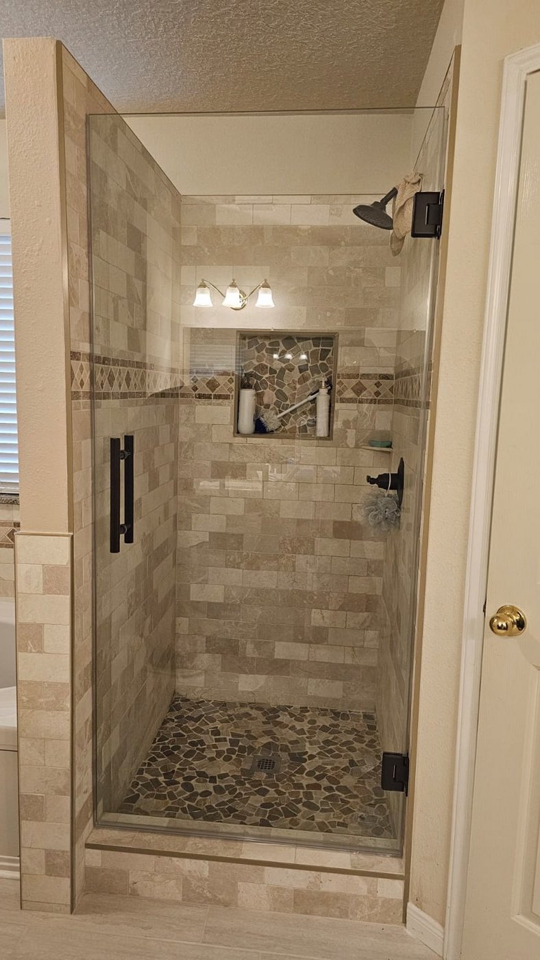 Single door con herraje negro instalada por Glas Plus en un shower de azulejo beige