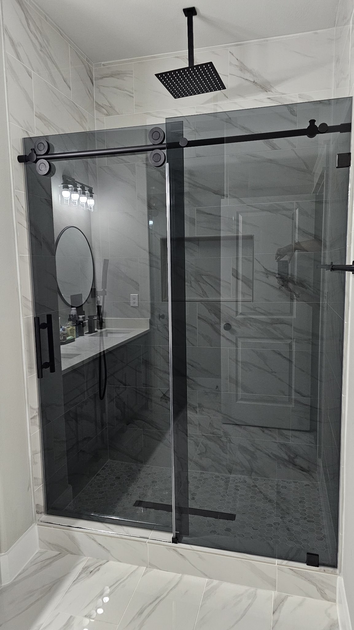 Sliding de una puerta con panel fijo, vidrio Grey (gris ahumado) y barra negra en shower de mármol con ducha de lluvia