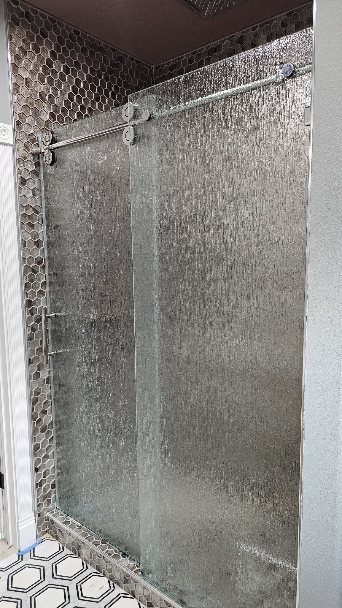 Sliding de una puerta con vidrio Rain (textura de lluvia), riel cromado y panel fijo en shower de azulejo hexagonal