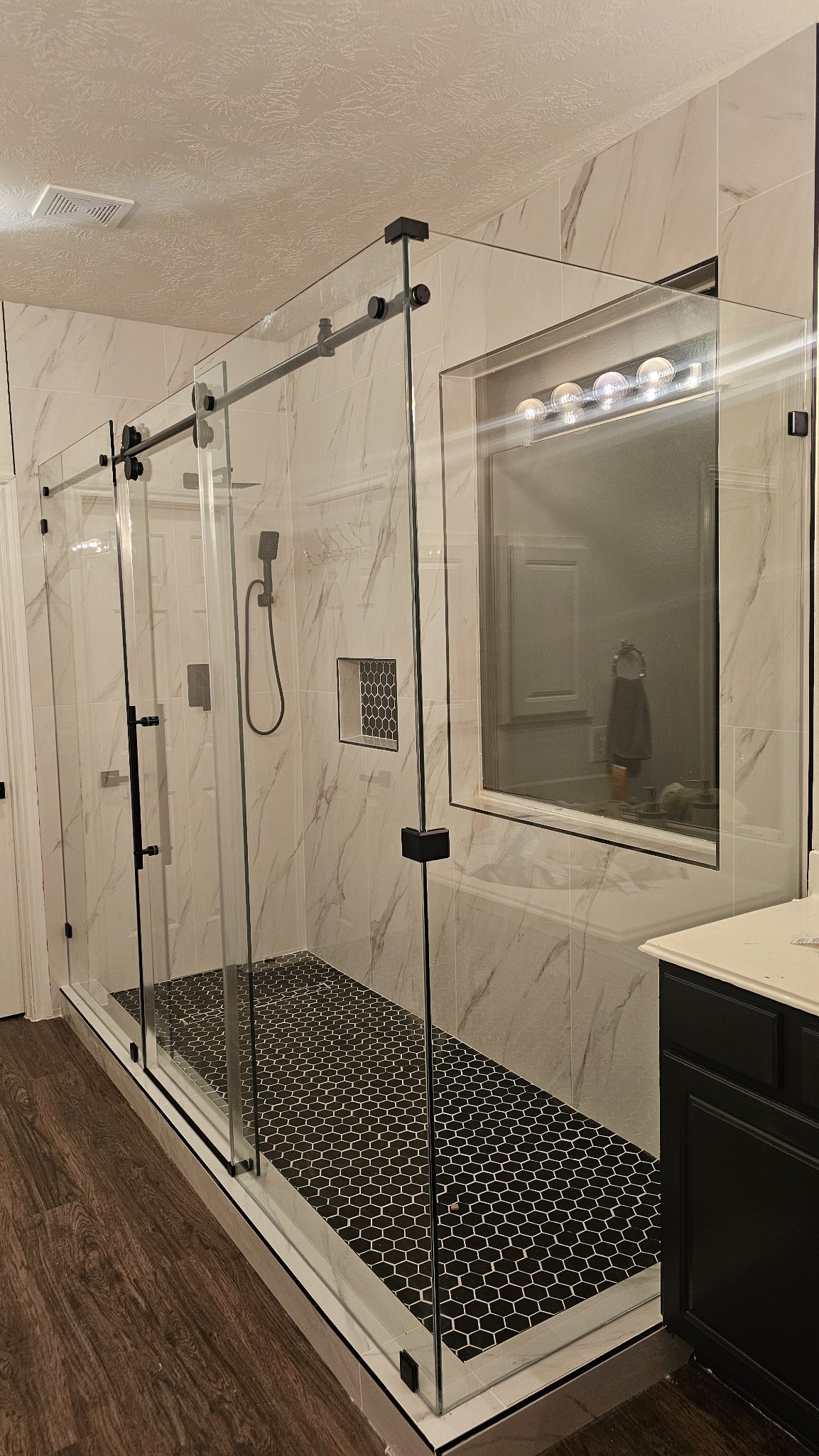 Ejemplo de sliding doble puerta de Glas Plus: dos puertas corredizas de vidrio sobre un riel con herraje negro, en un baño amplio de mármol