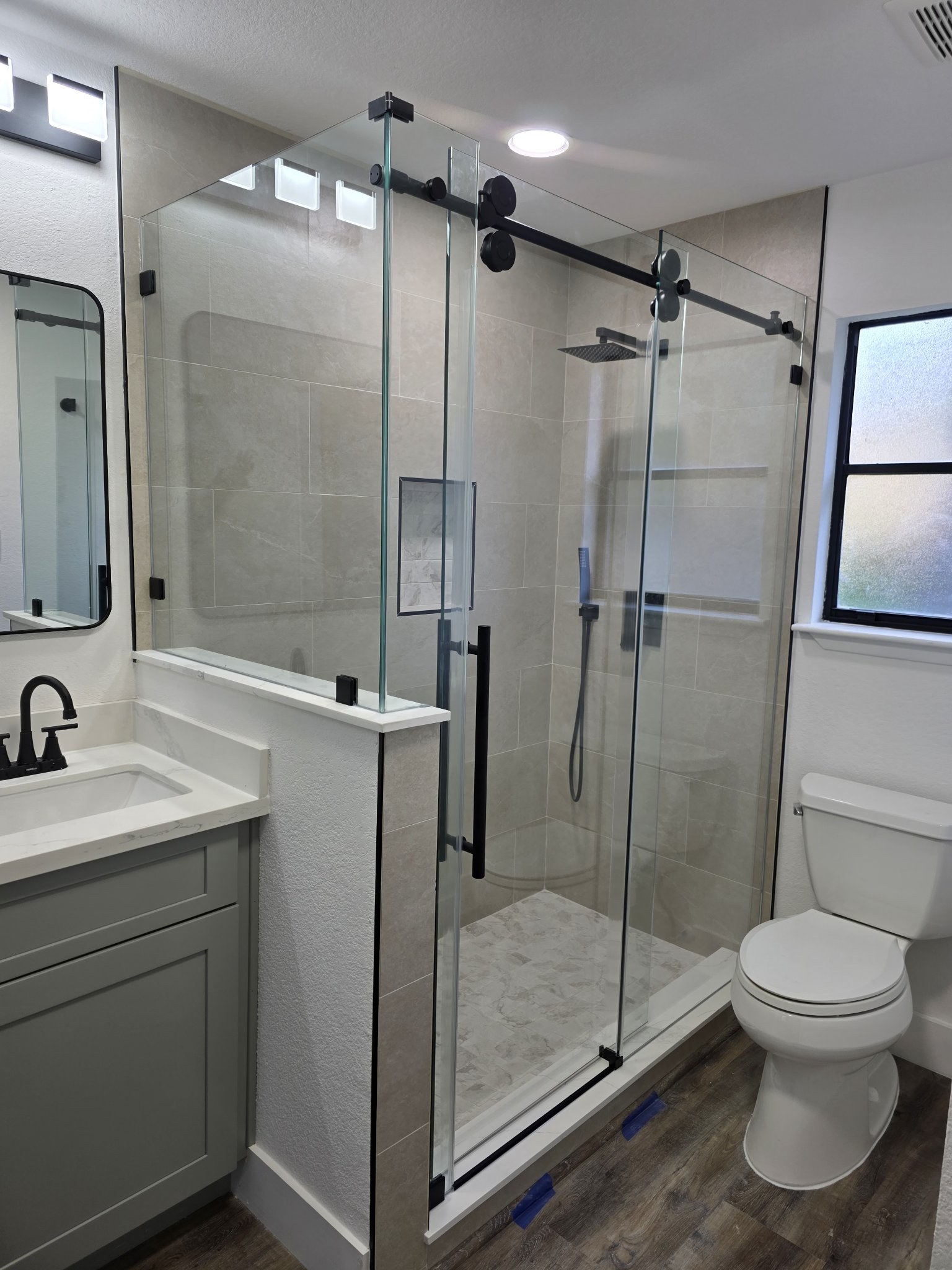Sliding con retorno sobre medio muro con riel negro en shower de azulejo beige