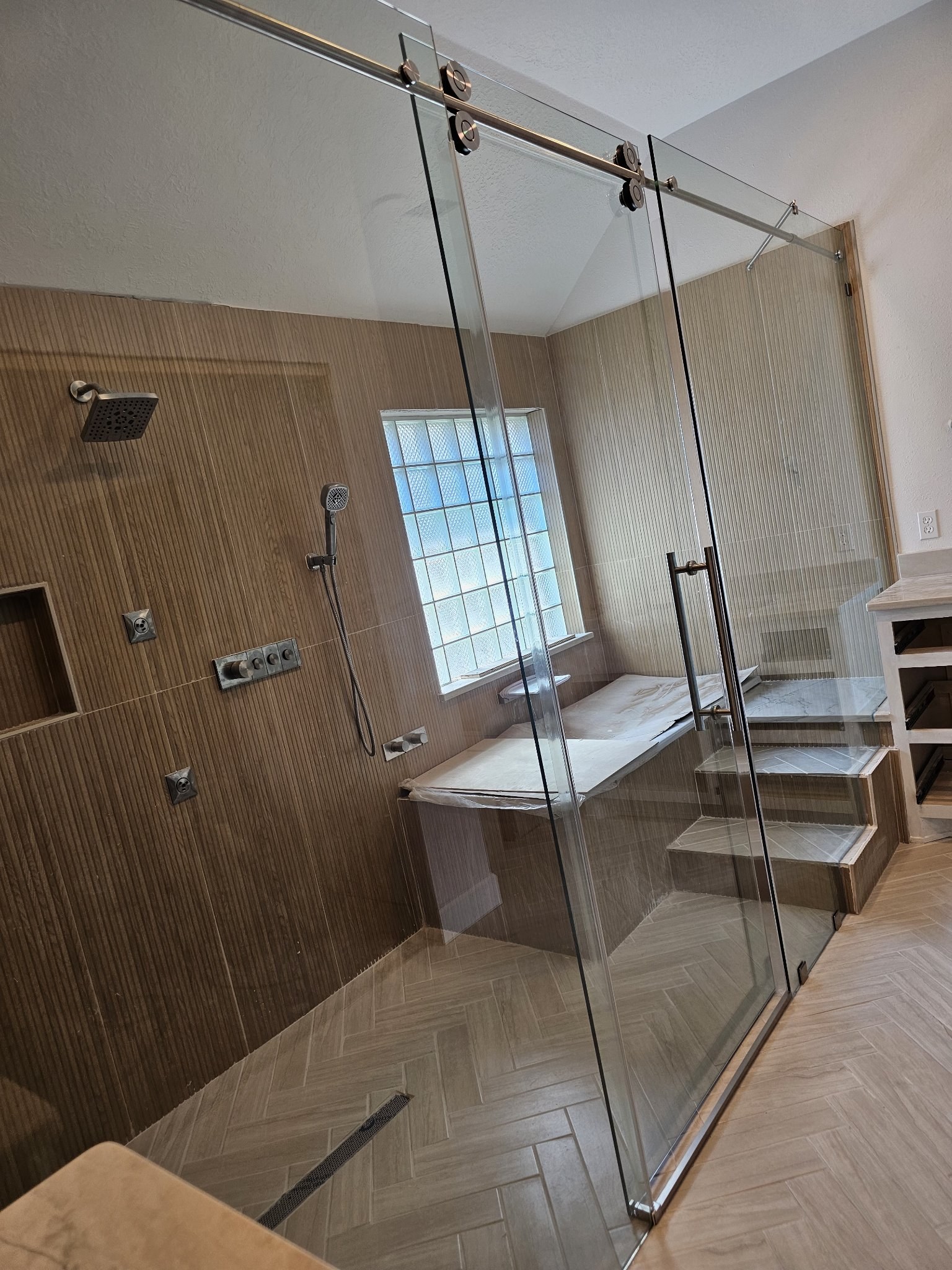 Sliding de una puerta con panel fijo y riel de brush nickel en shower amplio de azulejo tipo madera con banca y ventana de bloques de vidrio