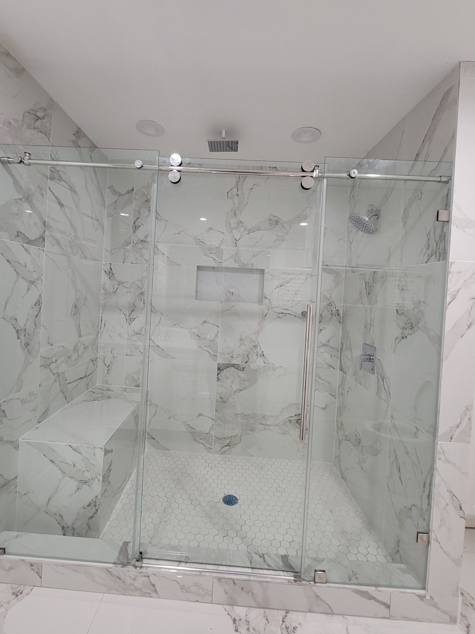 Sliding de una puerta con panel fijo y riel cromado en shower de mármol con banca y nicho