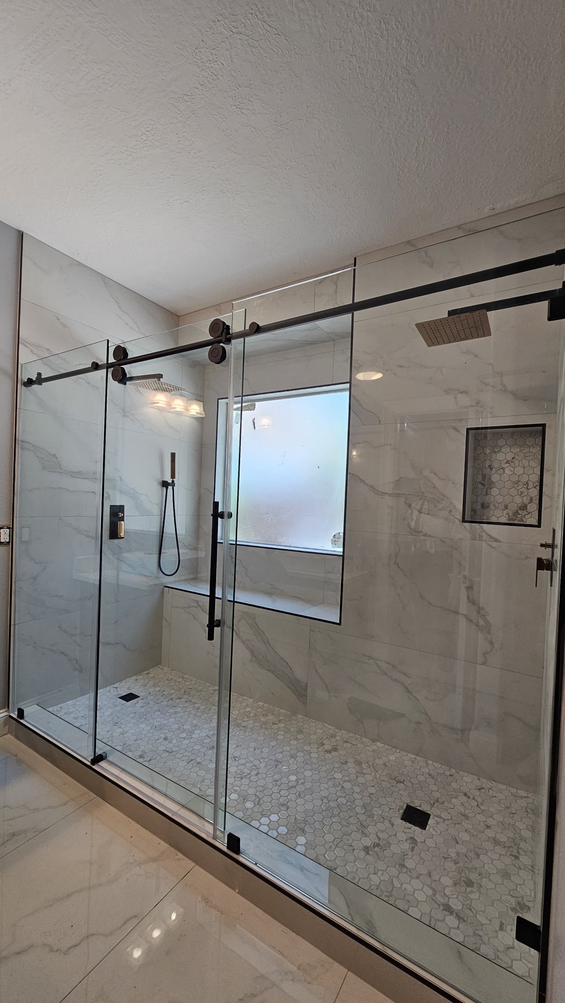 Sliding con puerta en el centro (panel fijo, puerta y panel fijo) con riel negro en shower de mármol blanco con ventana esmerilada y dos duchas