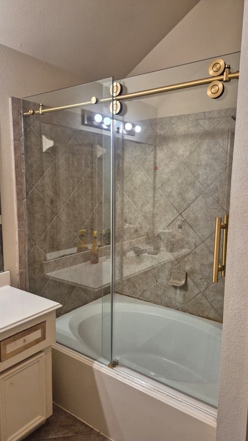 Sliding de una puerta con riel redondo dorado sobre tina en baño de azulejo beige