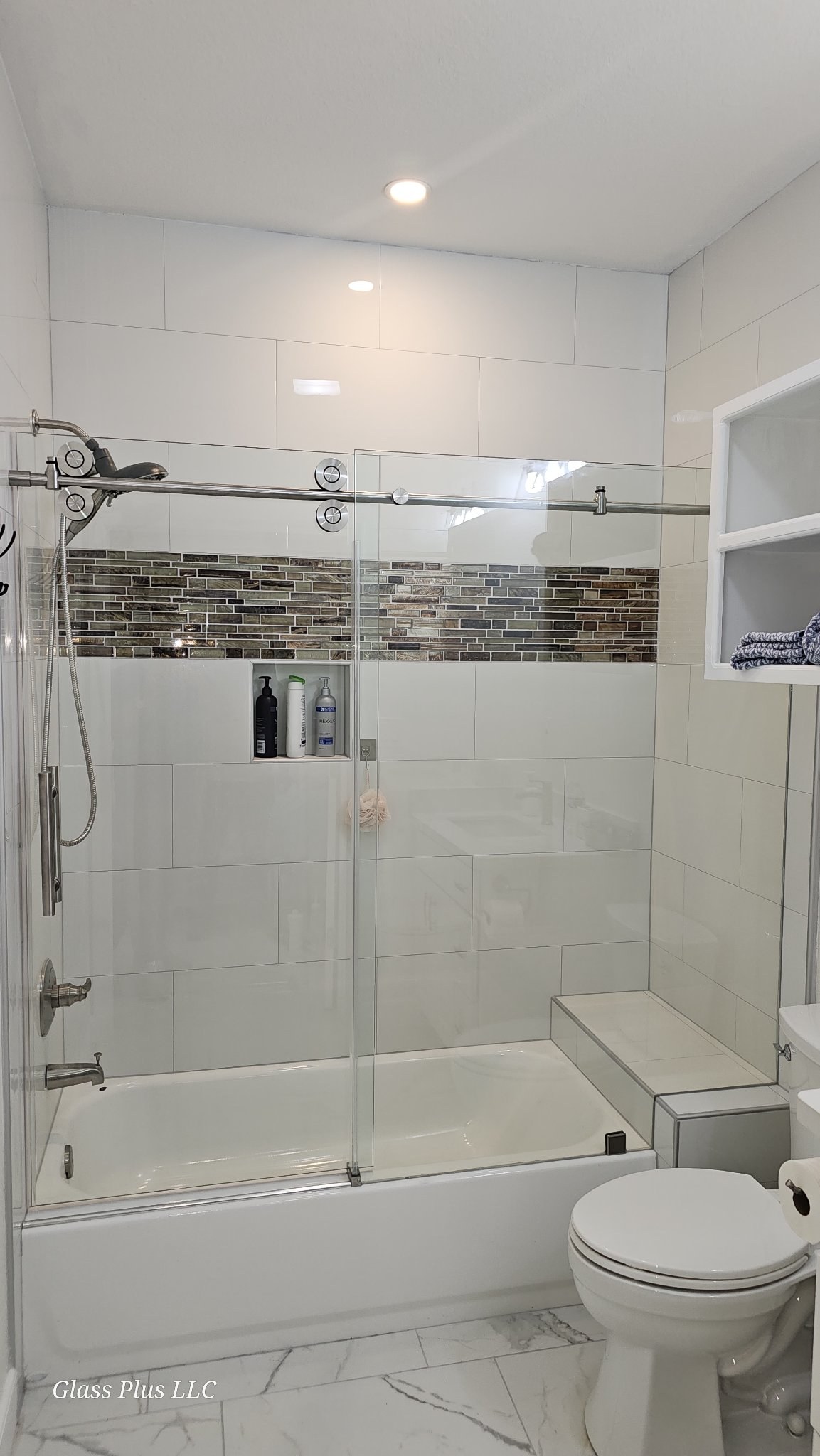 Sliding de una puerta con panel fijo y riel de brush nickel sobre tina en baño de azulejo blanco con franja de mosaico y nicho